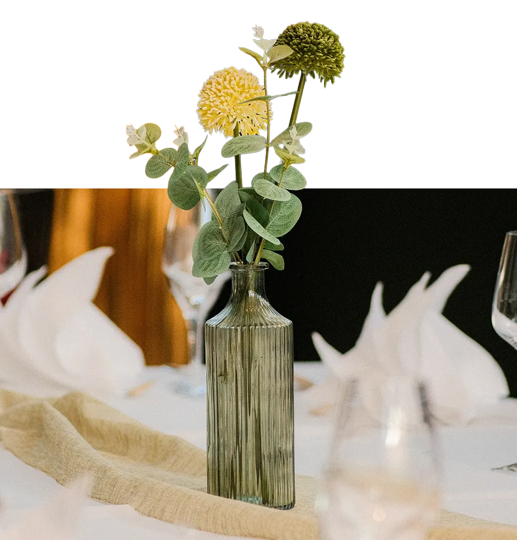 Kleine Glasvase mit gelb-grünen Blumen und Eukalyptus als Tischdekoration bei Kerzenlicht